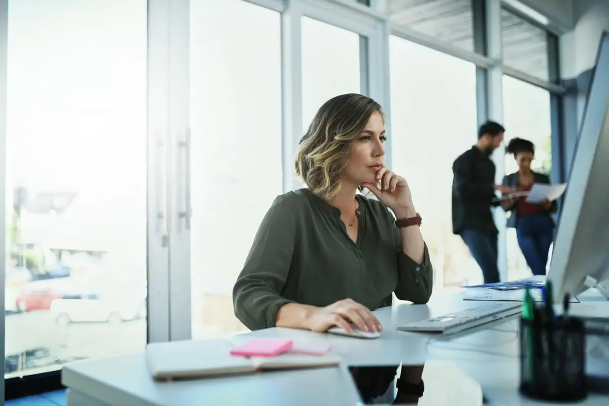 A woman works at a desk while movers handle paperwork in the background.
