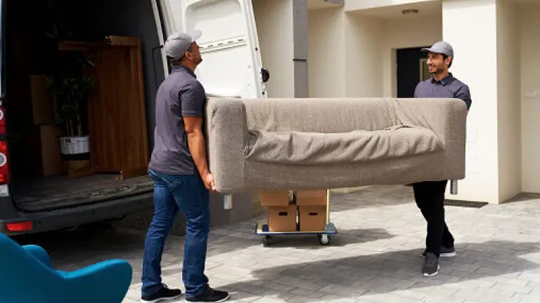 Two professional movers carrying a sofa from a home to a moving van.