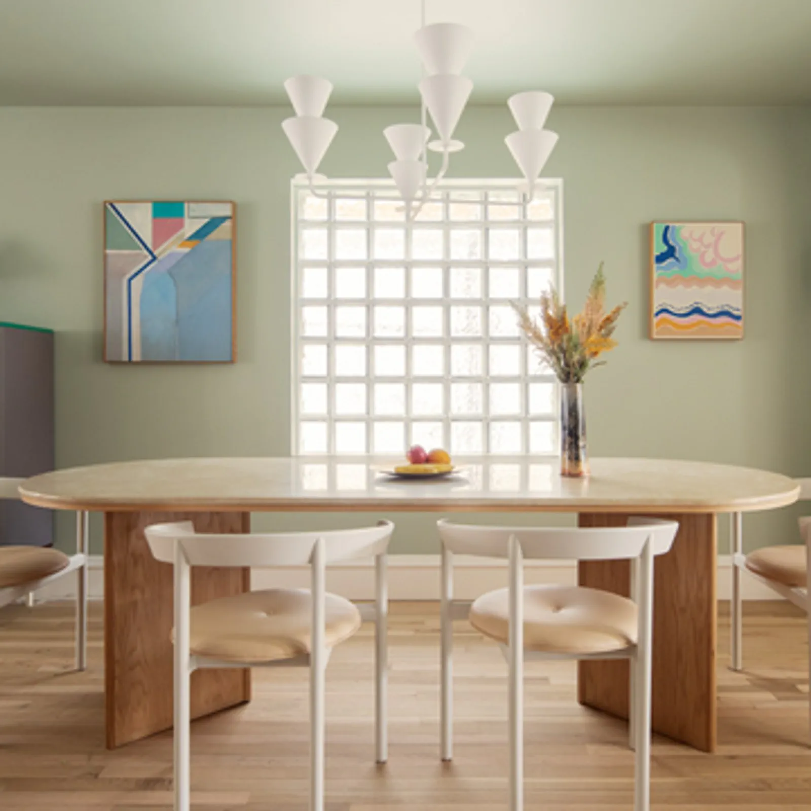 Modern dining area featuring a circular table, white chairs, artwork, and a vase with flowers.