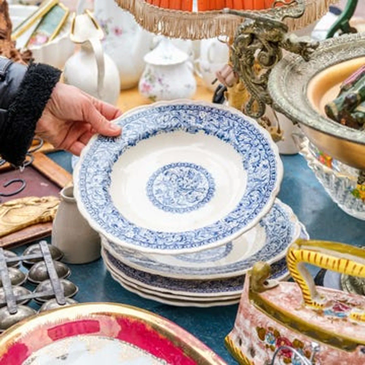 Woman Examines White Porcelain Plate at Outdoor Market Stall of Vintage Ceramics Handcrafted Collectibles Display