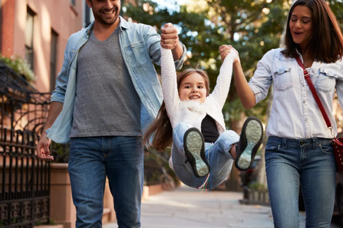 A young girl jumps up while holding both her parents’ hands after they successfully accomplished moving with kids.