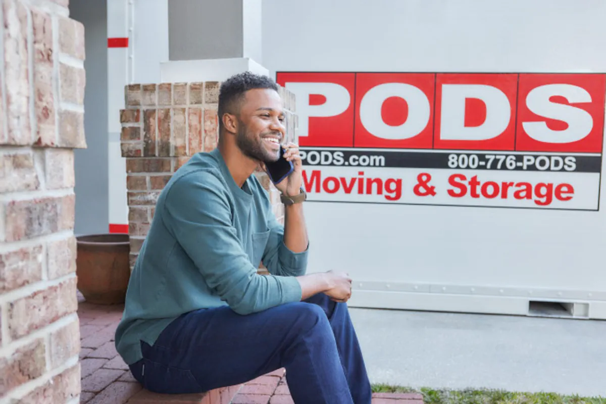 A man talks on the phone near a portable moving container.
