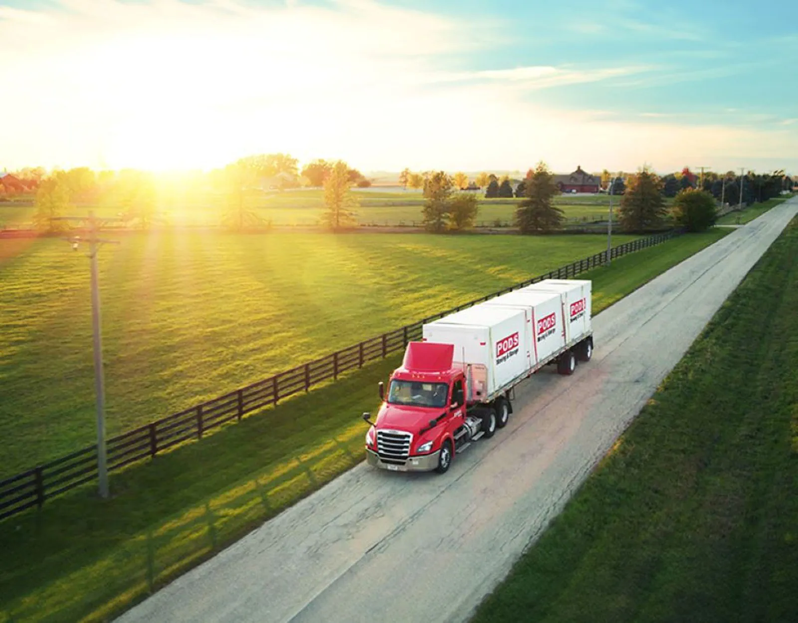 A moving truck carries portable containers along a rural road.