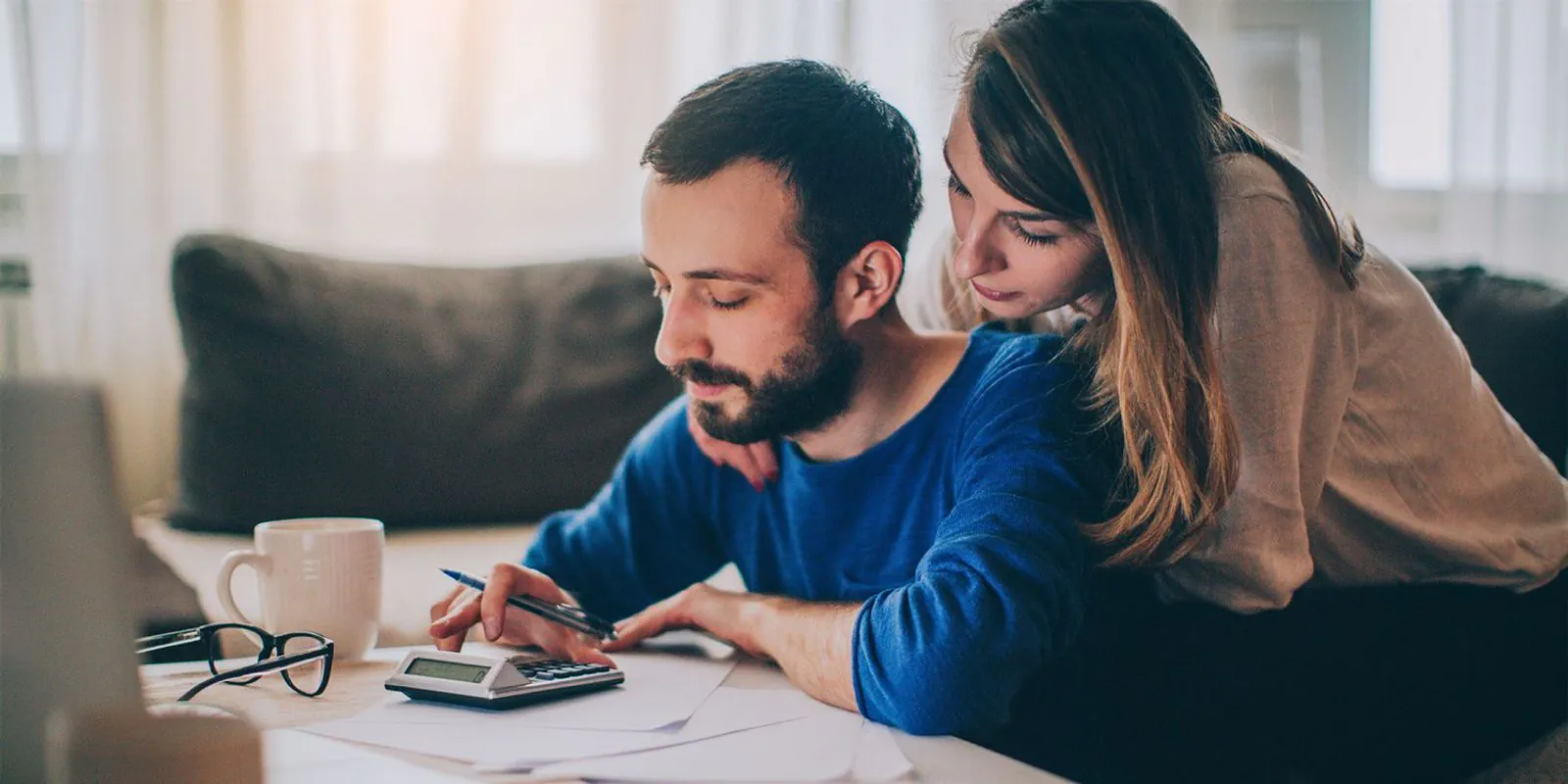 A couple organizes mortgage application paperwork and reviews costs with a calculator.