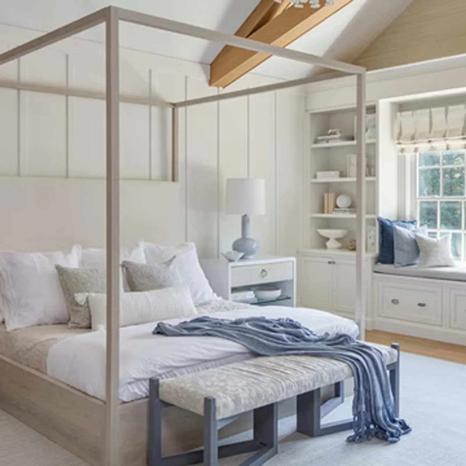 Bright and airy bedroom featuring a canopy bed, bedside tables, and a cozy window seat with decorative pillows.
