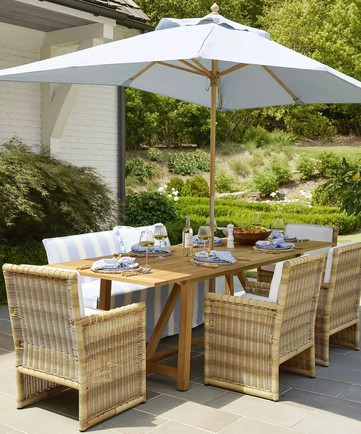 an outdoor dining scene with a table, an umbrella, chairs, a striped bench, and tableware set