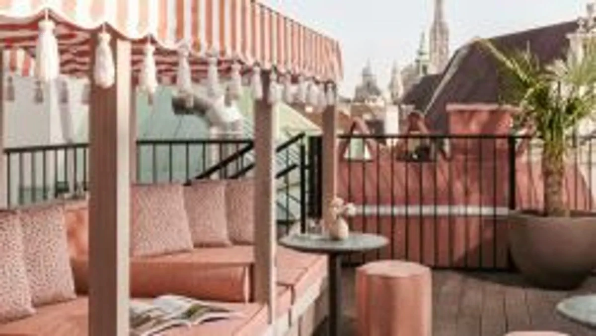 Flamingo pink cushioned terrace seating with a striped tassel-accent canopy and petite patio table