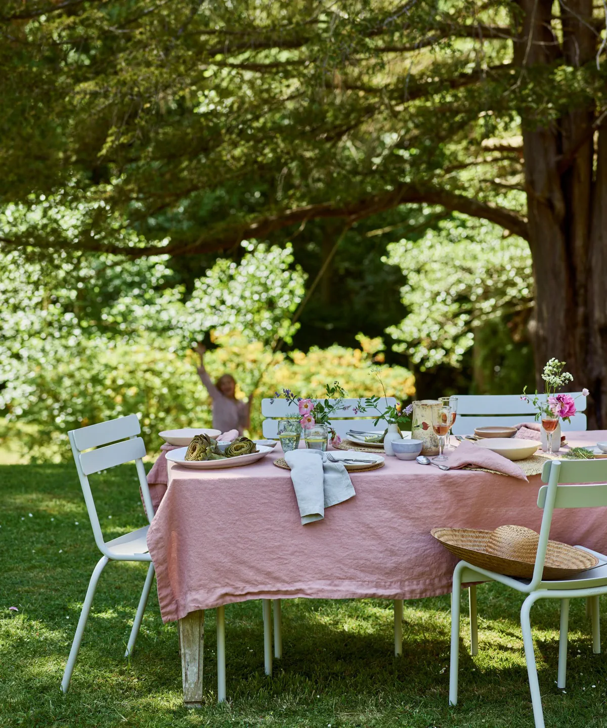 an outdoor dining scene with white chairs, a pink tablecloth, and decor on the table