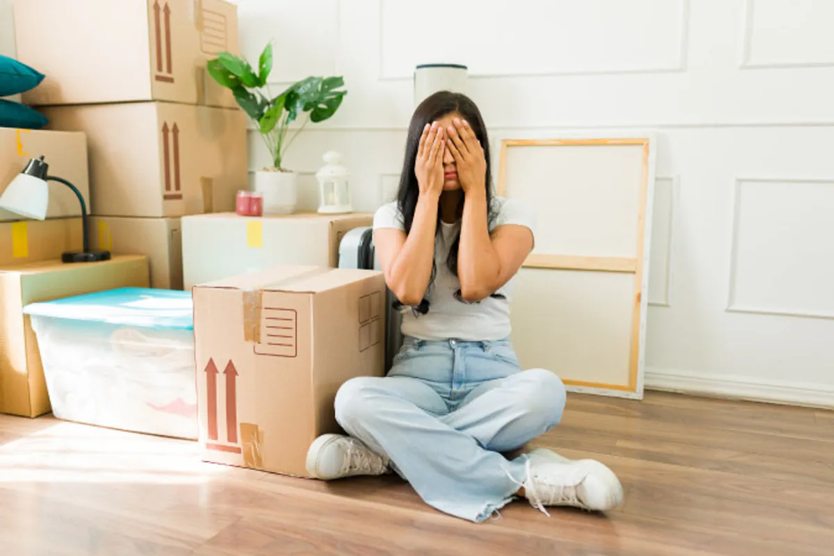 A woman sits beside moving boxes and looks overwhelmed.