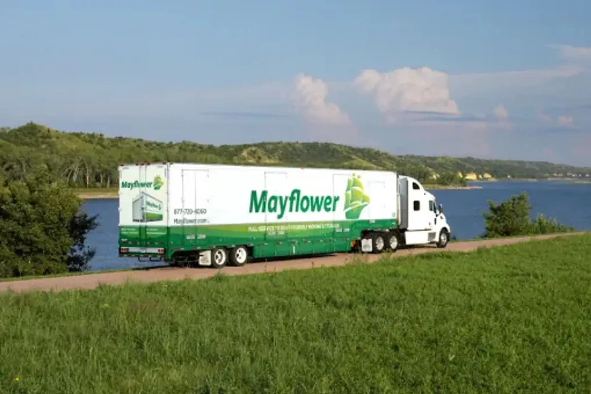 A mayflower truck driving along a highway next to a lake.