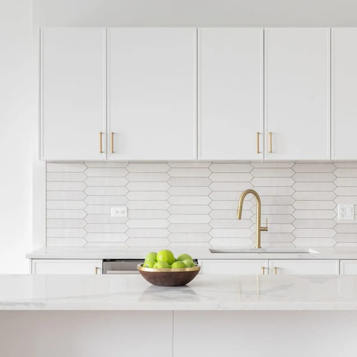 Close-up of a gold faucet against white cabinets and marble counters.